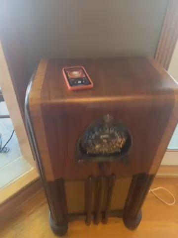 A fully restored 1938 Zenith Amp and Radio console featuring a glossy black dial, wood knobs, and a vintage push-pull speaker. Designed for hi-fi performance and Bluetooth connectivity, this elegant mid-century modern cabinet offers warm, authentic tones for music enthusiasts.