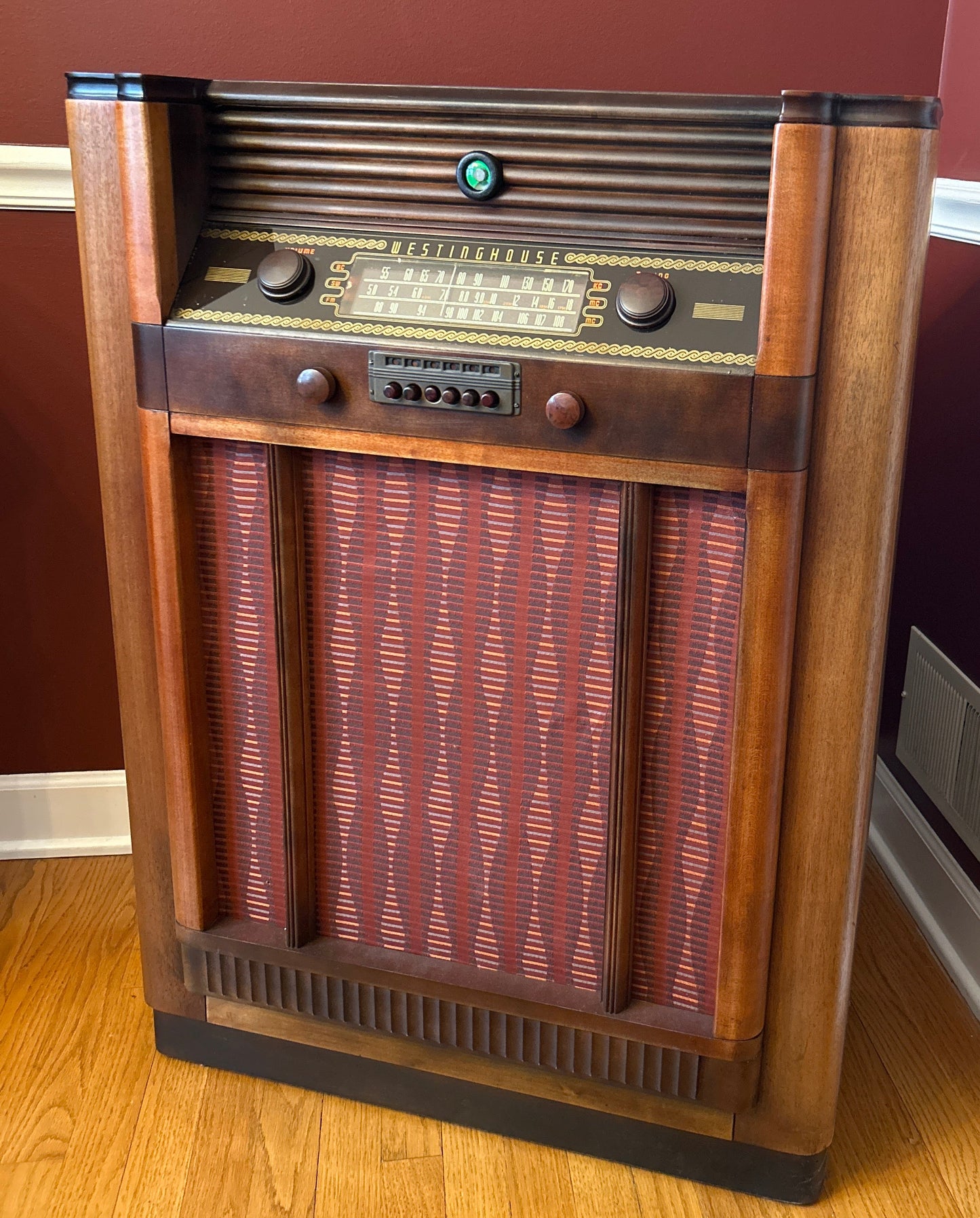 Vintage wooden radio on a wooden floor with a red wall in the background