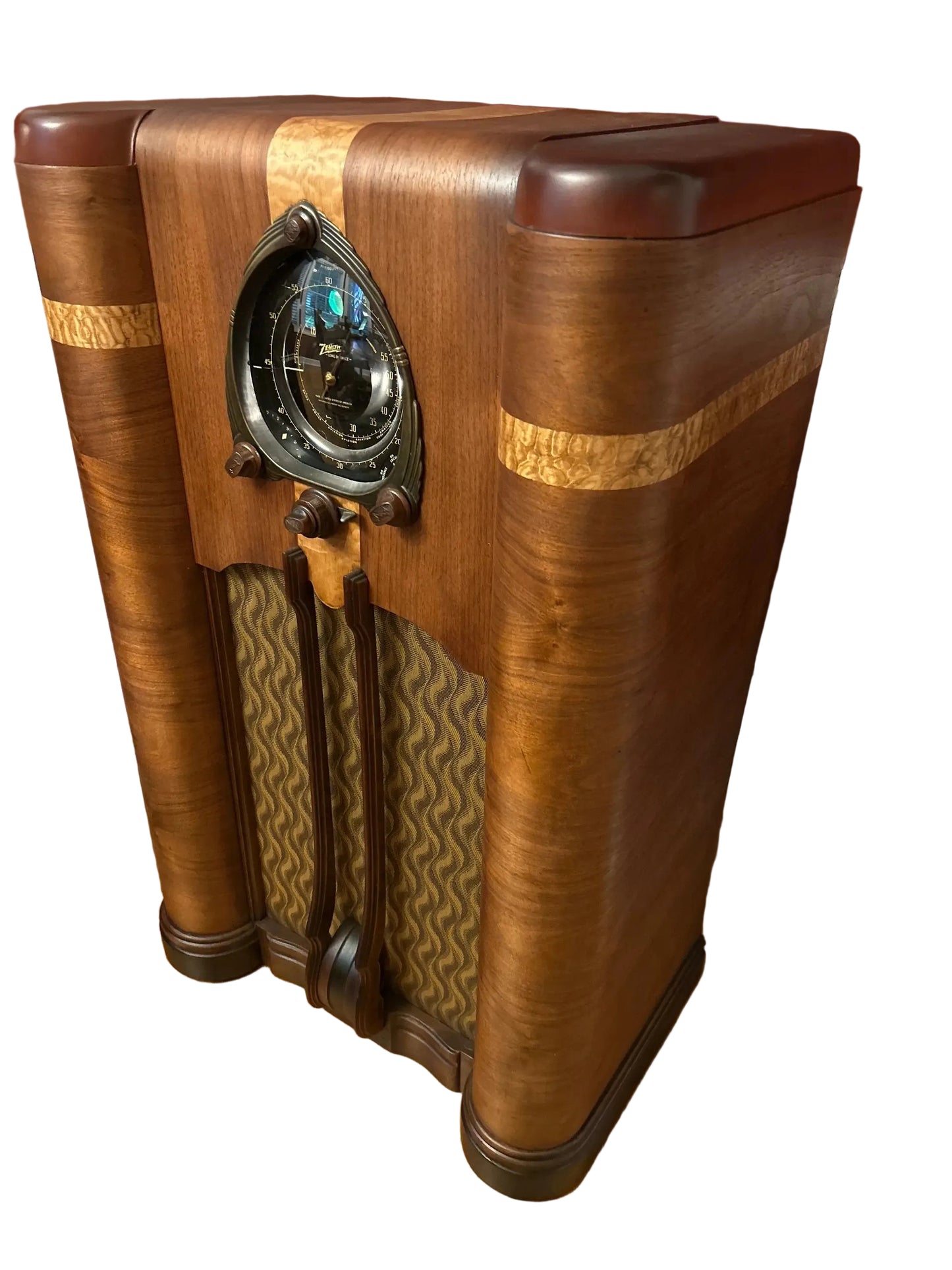 An antique Art Deco wooden radio cabinet with a polished mahogany finish, featuring a circular dial face, patterned fabric front panels, and decorative wood inlays, set on a hardwood floor against a dark red wall.