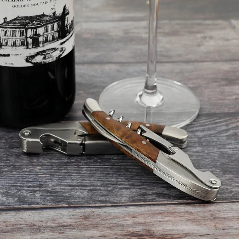 Wine bottle opener with wooden handle on a wooden surface next to a wine glass and bottle.